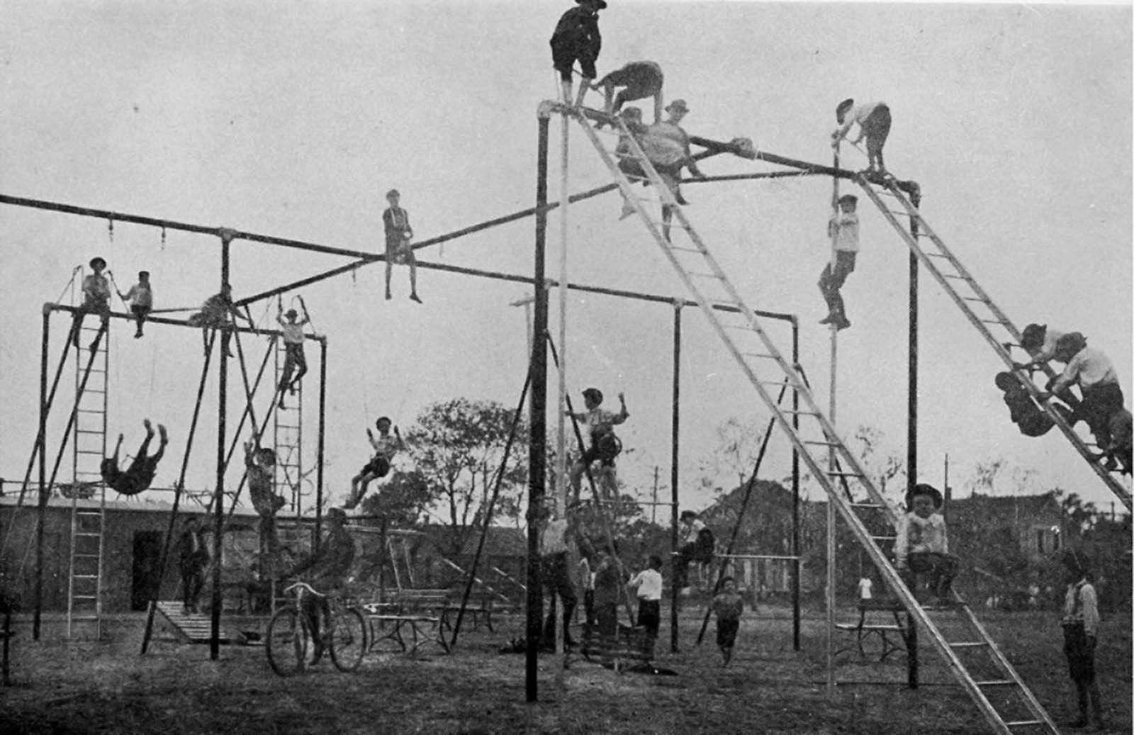 Black-and-white photograph of children climbing tall playground structures, ladders, and bars in an open lot.